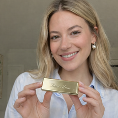 Woman holding a gold pillbox with 'Best Mom' engraving against a neutral background
