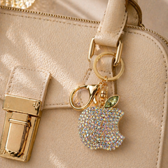 Beige handbag with a decorative keychain shaped like an apple with rhinestones.