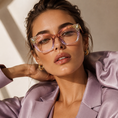 Woman wearing Swarovski crystal pink glasses with gold accents and a matching outfit against a neutral background