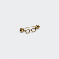 Gold-tone crystal eyeglasses holder pin on a cool gray background