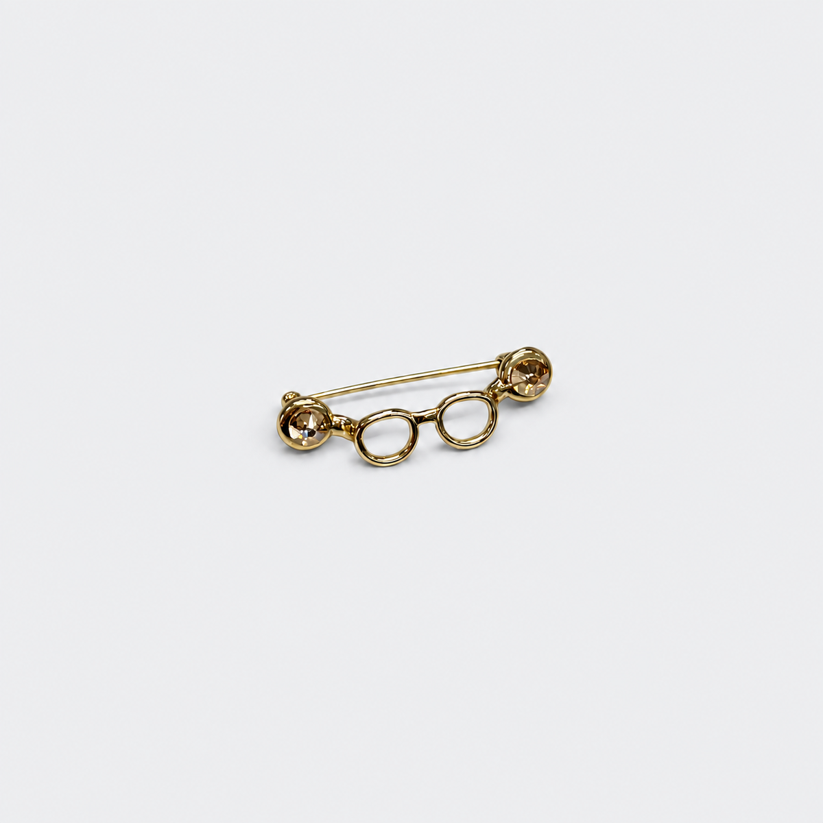 Gold-tone crystal eyeglasses holder pin on a cool gray background